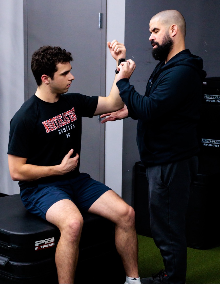 Jason Aguiar testing a seated athlete's shoulder strength with a handheld device