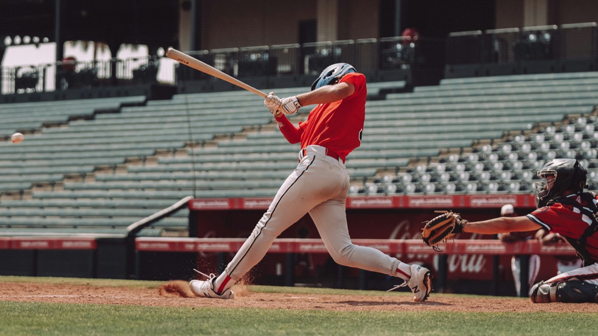 Baseball hitter in a red jersey swinging through a pitch at home plate