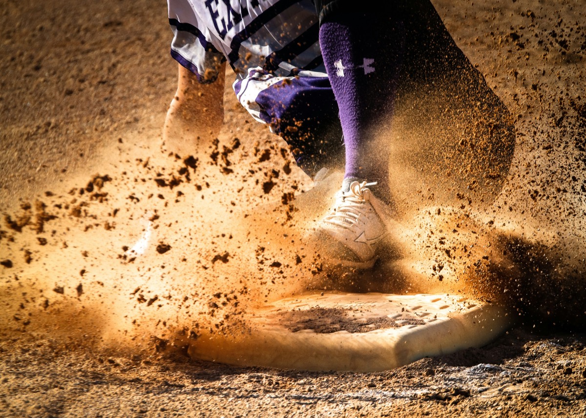 Close-up of a baseball player's cleat sliding into a base in a spray of dirt