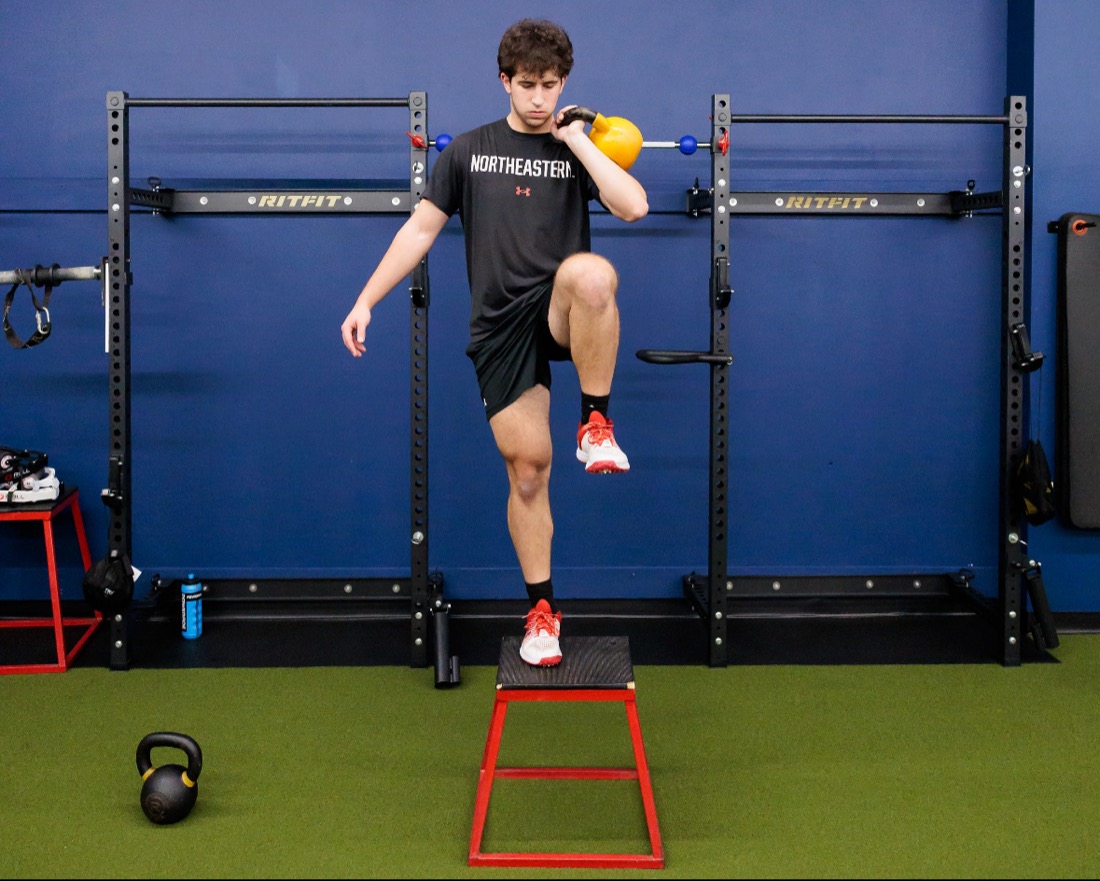 Baseball player doing a single-leg step-up while holding a kettlebell