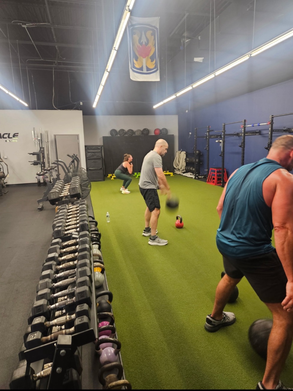 Adults doing kettlebell swings and goblet squats on the turf during a Pinnacle class