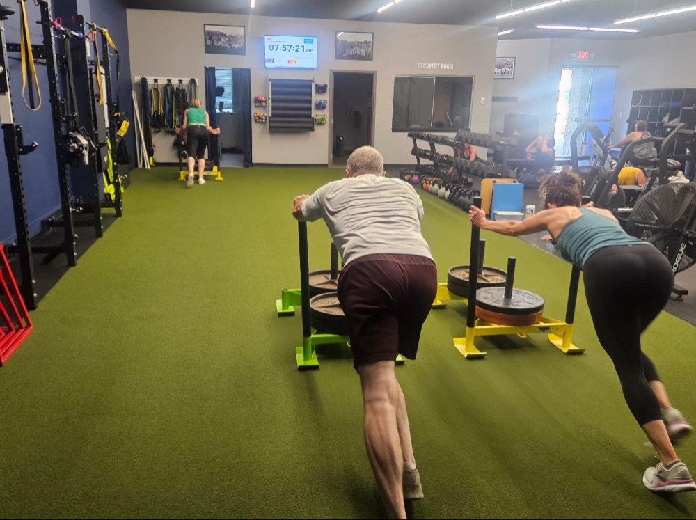 Adults pushing weighted sleds across the turf during a Pinnacle class