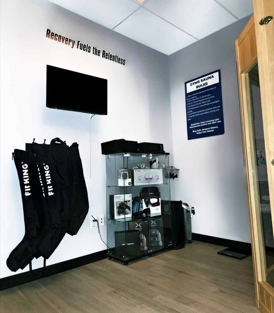 Leg compression boots hanging on the wall next to a case of Hyperice and massage gun recovery tools